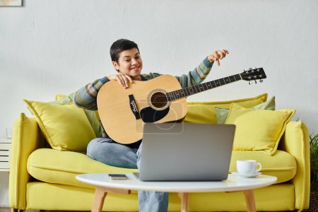 junge fröhliche Frau in lässiger Kleidung sitzt auf dem Sofa und lernt, wie man Gitarre in der entlegenen Klasse spielt