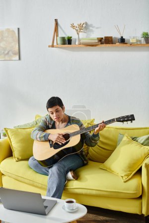 vertical shot of focused young woman sitting on sofa with guitar attending online music lesson
