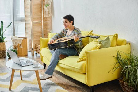 joyful attractive brunette woman holding guitar during remote music lesson, education at home