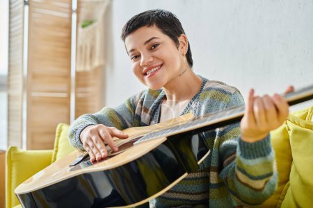 smiling young woman in casual attire attending remote guitar lesson and smiling at camera, education