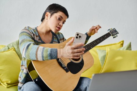 gut aussehende fokussierte Frau besucht Online-Gitarrenkurs mit Handy in der Hand, Ausbildung zu Hause