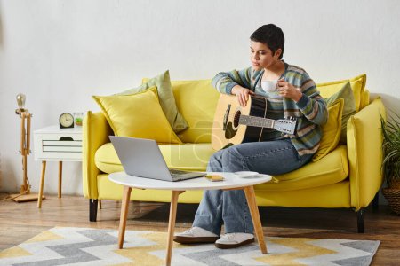 Téléchargez les photos : Jeune femme concentrée assise sur un canapé avec guitare pendant un cours de musique en ligne, éducation à la maison - en image libre de droit