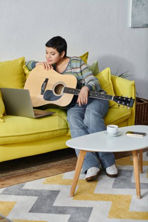Photo for Vertical shot of cheerful young woman sitting on sofa with guitar on remote music lesson, education - Royalty Free Image