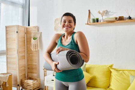 happy attractive woman in sportswear smiling cheerfully at camera with fitness mat in hands