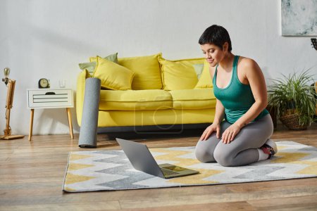 young sporty woman sitting on floor and looking at laptop before online class, fitness and sport