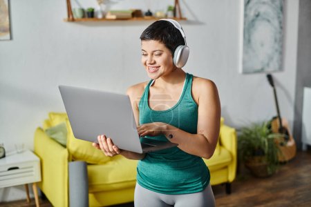 mujer joven feliz con el ordenador portátil y auriculares que asisten a la lección de fitness remota, fitness y deporte