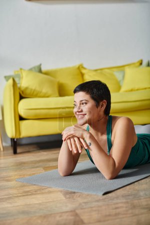 vertical shot of joyous woman with short hair and tattoo smiling and looking away, fitness and sport