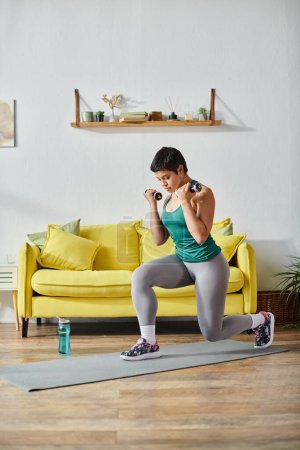 vertical shot of attractive young woman in sportswear doing lunges with dumbbells, fitness and sport