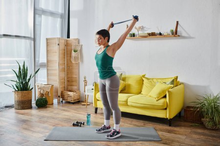 good looking brunette woman in comfy sportswear exercising actively with resistance band, fitness