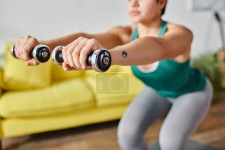 cropped view of young woman with tattoo on hand exercising actively with dumbbells, fitness