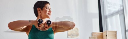 joyous woman with short hair exercising with dumbbells and looking away, fitness and sport, banner