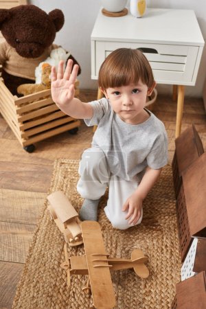 Foto de Tiro vertical de adorable niño jugando con juguetes de madera y saludando a la cámara, familia - Imagen libre de derechos