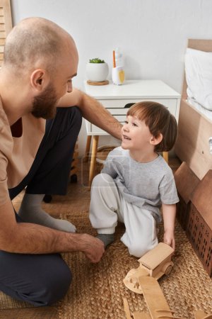 Photo for Cheerful little boy smiling at his bearded father while they playing with wooden toys, family - Royalty Free Image