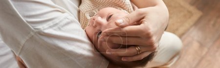 cute newborn baby boy lying peacefully in arms of his mother, hand on head, family concept, banner
