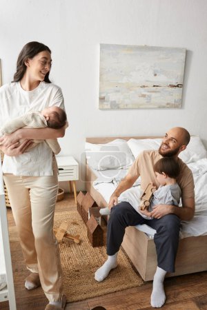 vertikale Aufnahme moderner Eltern, die einander fröhlich anlächeln, während sie Zeit mit Kindern verbringen