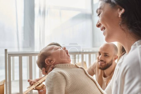 Photo for Focus on happy mother looking at her newborn baby with blurred joyful father on backdrop, family - Royalty Free Image