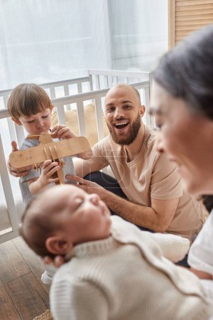 Photo for Focus on bearded father playing with his son and looking at his blurred wife holding their baby boy - Royalty Free Image