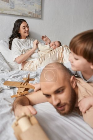 Photo for Focus on happy mother holding her newborn baby boy next to her blurred husband and little son - Royalty Free Image