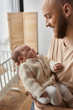 vertical shot oh jolly bearded man looking lovingly at his newborn baby boy while holding him