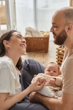 Photo for Vertical shot of happy couple smiling at each other and holding their newborn baby boy, family - Royalty Free Image