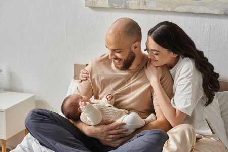 glückliches modernes Paar, das sich umarmt und liebevoll auf seinen entzückenden neugeborenen Jungen blickt, Familienkonzept