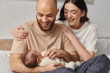 Photo for Good looking modern parents hugging and holding their newborn baby in arms smiling joyfully, family - Royalty Free Image