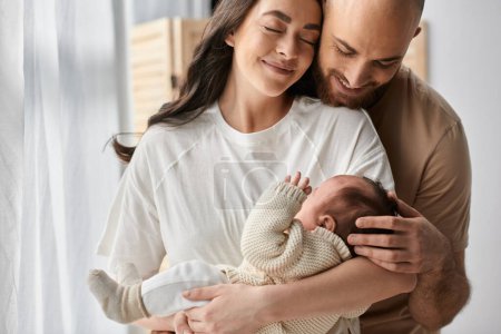 Photo for Joyous modern parents in cozy homewear hugging warmly and holding their newborn son lovingly, family - Royalty Free Image