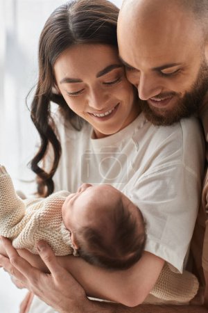 Photo for Vertical shot of loving modern parents hugging and smiling at their newborn baby boy, family - Royalty Free Image