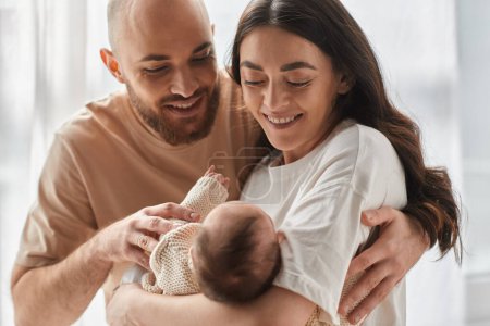 Photo for Joyous happy parents in cozy homewear smiling happily at their newborn baby boy, family concept - Royalty Free Image