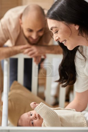 focus on joyous mother putting her newborn baby into crib with her blurred husband looking at them