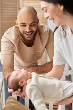 vertical focused shot of bearded happy father looking at his blurred wife holding their newborn baby