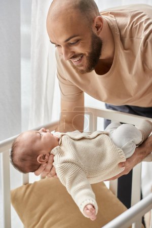 vertical shot of bearded happy father putting his newborn son into his crib, family concept
