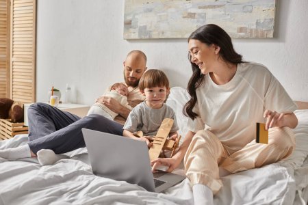 happy loving family spending time together in bed with laptop and credit card, modern parenting