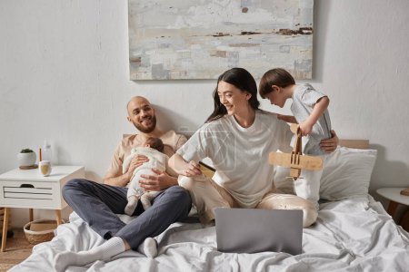 happy beautiful family spending time together in bed with laptop and credit card, modern parenting