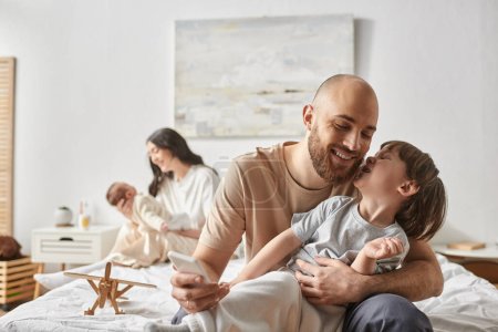 focus on joyful father and his little son having fun next to his blurred wife and baby on backdrop
