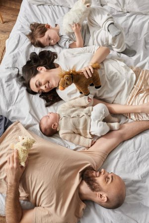 top view of attractive modern parents lying on bed with their newborn baby and little son, family