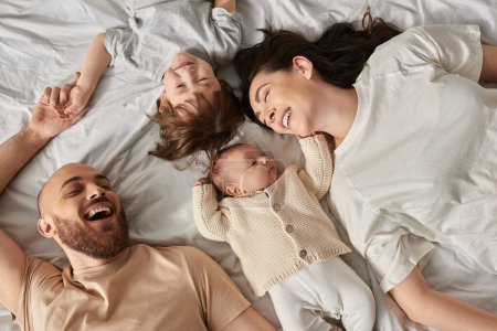 top view of happy relaxing family in cozy homewear lying on bed together, modern parenting