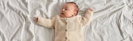 vista superior de adorable bebé recién nacido niño acostado en la cama en casa con los brazos ligeramente levantados, pancarta