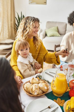 happy mother sitting with daughter and holding hands while praying at Thanksgiving table, gathering