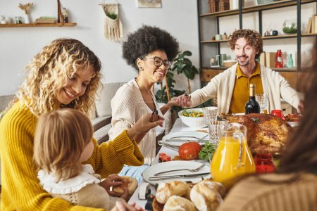 happy multiracial family holding hands and praying at Thanksgiving table, thankful for meal