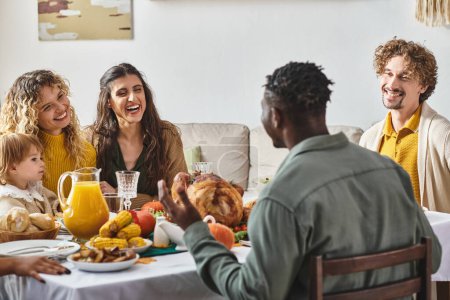 fröhliche multiethnische Freunde reden in der Nähe von Kleinkind Mädchen während Thanksgiving-Feier, Festtag