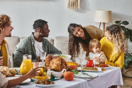 happy interracial people looking at cute toddler baby during Thanksgiving celebration at home