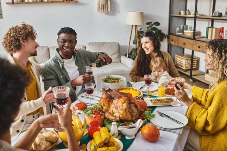 familia multicultural disfrutando de la cena de Acción de Gracias en la mesa festiva, madre e hijo cerca del pavo