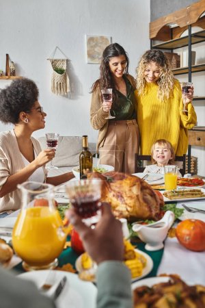 Thanksgiving holiday, happy lgbt couple cheering glasses of wine near cute toddler baby