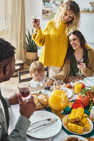 joyful lgbt couple celebrating Thanksgiving with toddler baby girl, cheering and laughing at home