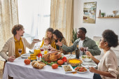happy man passing plate with roasted potatoes to african american friend during Thanksgiving dinner Poster #678866622