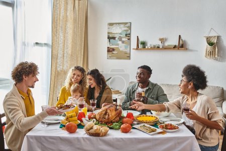 man passing plate with roasted potatoes to happy african american woman during Thanksgiving dinner