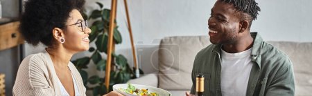 happy african american woman passing bowl with salad to relative during Thanksgiving dinner, banner