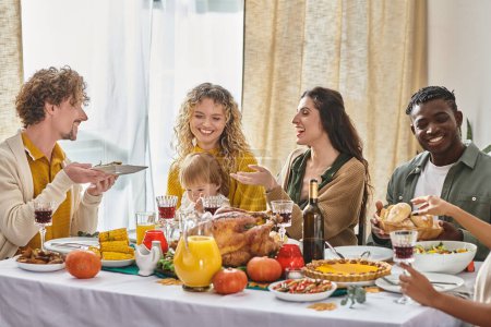 happy multiracial family and friends gathering at Thanksgiving table with various meals and drinks