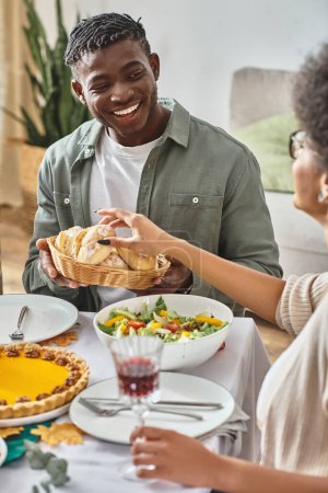 feliz afroamericano hombre mirando hermana tomando bollo horneado durante día de fiesta de Acción de Gracias